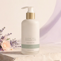 Trinidy MK Cloud Veil Hydrating Body Lotion pump bottle on a cream pedestal with lavender and peach florals