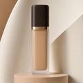 Trinidy MK Soft Focus Skin Tint bottle standing on a warm neutral studio pedestal